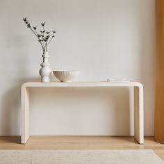 a white vase with flowers sitting on top of a wooden table next to a bowl