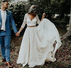 a bride and groom holding hands walking through the woods in their wedding attire, with one man wearing a blue suit