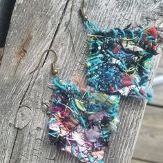 two pieces of fabric are hanging on the side of a wooden fence, one is colorful