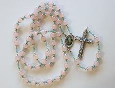 Guardian angel Catholic Rosary lovingly handmade from Coral Pink Jade Gemstone beads (8mm). Rosary centre features Guarding Angel (20mm x 12mm) Very ornate rosary with each bead surrounded in floral bead caps and smoky light blue 3mm crystal beads. Crucifix with Hearts is featured. (45mm x 30mm) Total Length 62cm.  This rosary is presented in a vegan leather pouch, and is gift boxed with a ribbon and a gift tag. We also include some relevant prayer cards, and a "how to pray the rosary" leaflet.  If you would like to customise your rosary, we can add a name to the rosary in silver beads.  Proceeds from the sale of our rosaries go towards making Children's Rosaries for children in our local parish and for parishes around the globe. (See our instagram page for more). Spiritual Rosary As Valentine's Day Gift, Mother's Day Rosary With 8mm Beads, Mother's Day Gift Rosary With 8mm Beads, Gift Rosary With Round Natural Stones, Round Beads Rosary With Natural Stones For Gift, Mother's Day Spiritual Rosary, Gemstone Beads Rosary As Gift, Pink Jade, Praying The Rosary