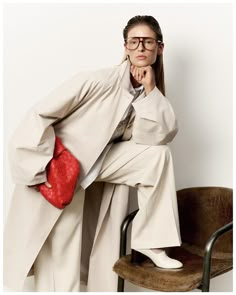 a woman sitting on top of a chair with a red purse in her hand and looking at the camera