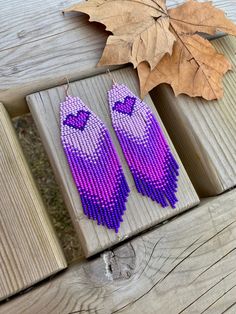 two purple beaded owl earrings sitting on top of a wooden bench next to a leaf