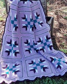 a purple crocheted blanket sitting on top of a wooden bench in the grass