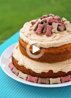 a cake with white frosting and pink and brown dog biscuits on top sits on a blue tablecloth