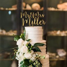 a wedding cake with white flowers and greenery on the top is decorated with mr and mrs's name