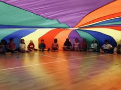 a group of children sitting on the floor in front of colorful umbrellas at a school