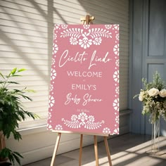 a pink welcome sign sitting on top of a wooden easel next to a plant