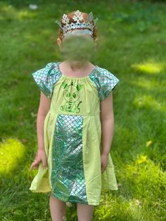 We make Kids dress-up clothes that are real garments you can wash and wear for years. The elastic neckline and sleeves, and flowing pattern means kids can wear the same dress from age 2 up to age 5+.   For this dress,  hand dyed cotton from new cotton sheets is the primary fabric with shinny dragon scale fabric for sleeves and front detail.  Adorable dragon on the front is a foil Cricut design. Dress comes  with a paper crown with  gold elastic head band. Spring Green Princess Dress With Short Sleeves, Summer Costume Dress With Short Sleeves, Short Sleeve Summer Costume Dress, Green Princess Dress For Summer Dress-up, Whimsical Princess Dress For Summer Fancy Dress, Whimsical Summer Princess Dress For Fancy Dress, Green Summer Costume Dress, Green Princess Short Sleeve Dress, Green Fancy Dress For Summer