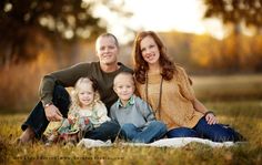 a family sitting in the grass with their two children and an adult posing for a photo