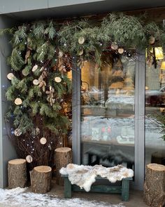 a bench sitting in front of a store window covered in snow and evergreen branches with ornaments hanging from the windows