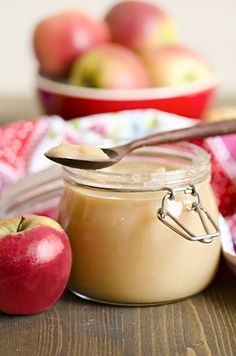 an apple and peanut butter in a glass jar with a spoon next to it on a wooden table