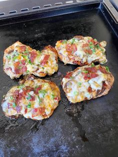 four small pizzas sitting on top of a black grilling pan covered in cheese and toppings