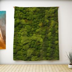 a green wall hanging on the side of a white wall next to a potted plant