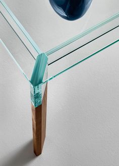 a glass table with wooden legs and a blue vase on the wall in the background