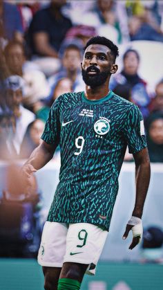 a soccer player in green and white uniform with his hand on his hip while looking up at the crowd