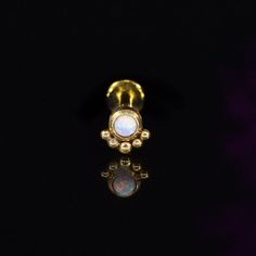 a gold nose ring with an opal stone in the center on a black background