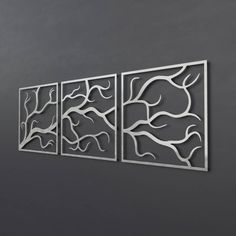 three metal wall art pieces hanging on the side of a gray wall in an empty room