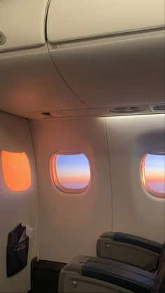 the inside of an airplane with two windows and some bags on the seat, looking out at the sunset