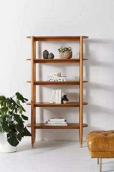 a wooden shelf with books and plants next to a leather chair in a white room