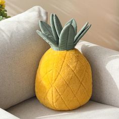 a yellow pineapple shaped pillow sitting on top of a gray couch next to a potted plant