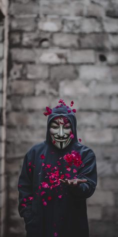 a person wearing a mask and holding flowers in front of their face while standing next to a brick wall