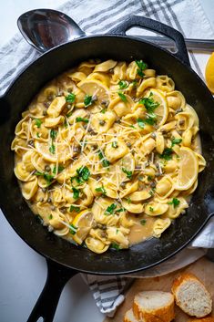 a skillet filled with pasta and cheese on top of a table next to sliced bread