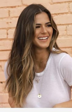 a woman standing in front of a brick wall with her hand on her hip and smiling at the camera