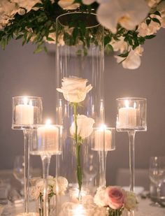 white flowers and candles are arranged in tall glass vases