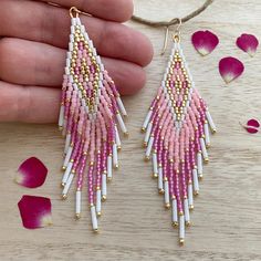 a pair of pink and white beaded earrings on a wooden table with rose petals