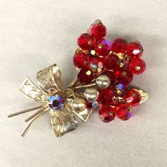 "Vintage era: 1950s Color: Red / Rainbow, Gold Closure:  Pin with safety clasp - Red Faceted beads with AB rainbow lustre  - Red AB rhinestones  - Gold-tone metal - Perforated Hearts on Ribbon Bow - feather shapes under flowers ✂------ M E A S U R E M E N T S -------    2.5\" tall 1.5\" wide 1\" pin 🔎--------- C O N D I T I O N  ------- Good condition Notes: just a bit of aging or tarnish to the metal finish, mostly on the heart perforated bow.  All of our items are vintage and have been handled well while in our care. We rarely have the item history and/or the storage method used before it was donated to us. We do our best to describe any problems with each piece. Please send us a message with any questions you may have about an item as we DO NOT accept returns!" Red Retro Brooch Jewelry, Retro Red Brooch Jewelry, Vintage Red Wedding Brooches, Vintage Wedding Brooches For Valentine's Day, Red Rhinestone Brooches For Wedding, Red Rhinestone Wedding Brooches, Vintage Red Brooches For Party, Feather Shapes, Vintage Bouquet