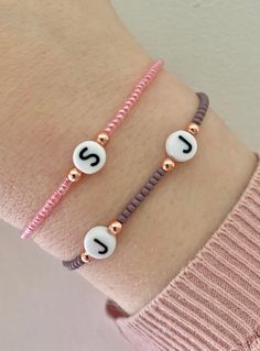 two bracelets with the letter j on them and beaded beads in white, pink, and gold