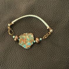 a bracelet with turquoise and brown beads sitting on top of a black leather surface,