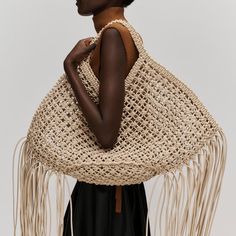 a woman is holding a woven bag with tassels on her shoulders and hands behind her back