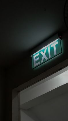 an exit sign is lit up in the dark with white letters on it and a black clock