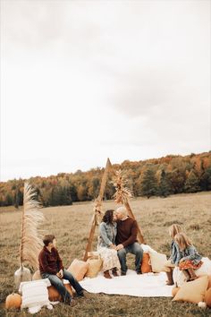 four people sitting on a blanket in an open field