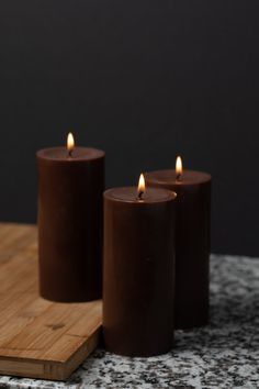 three purple candles sitting on top of a wooden cutting board