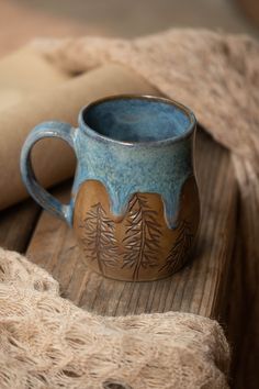 a blue and brown mug sitting on top of a wooden table next to a roll of paper