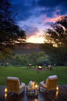 two chairs sitting on top of a wooden deck in front of a lush green field