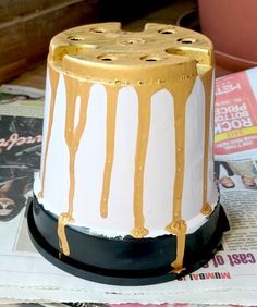 a white and gold decorated cake sitting on top of a newspaper next to a potted plant