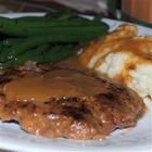 a white plate topped with meat covered in gravy and sliced avocado