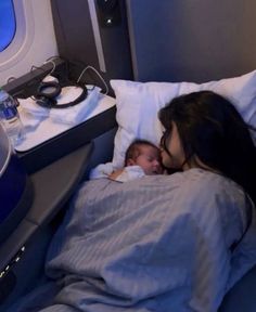 a woman is sleeping with her baby in the bed next to an air plane window