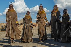 four people in brown clothing standing next to each other on a dirt ground with clouds in the background