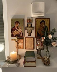 a shelf with pictures and candles on top of it in front of a wall mounted cross