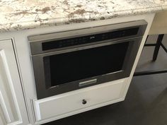 an oven built into the side of a kitchen counter with white cabinets and marble top