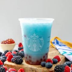 a blue drink with berries and raspberries on a cutting board next to it