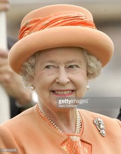 the queen is wearing an orange hat with pearls on her neck and she is smiling