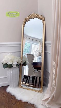 a large mirror sitting on top of a wooden floor next to a vase filled with flowers