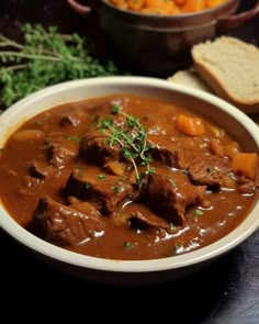 a bowl filled with meat and carrots next to bread