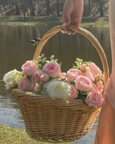 a person holding a basket full of flowers near the water's edge with ducks in the background