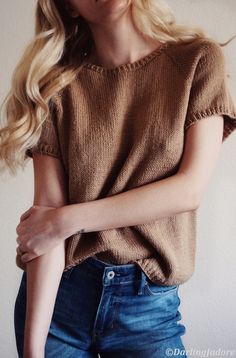 a woman with long blonde hair is wearing jeans and a brown sweater, posing for the camera